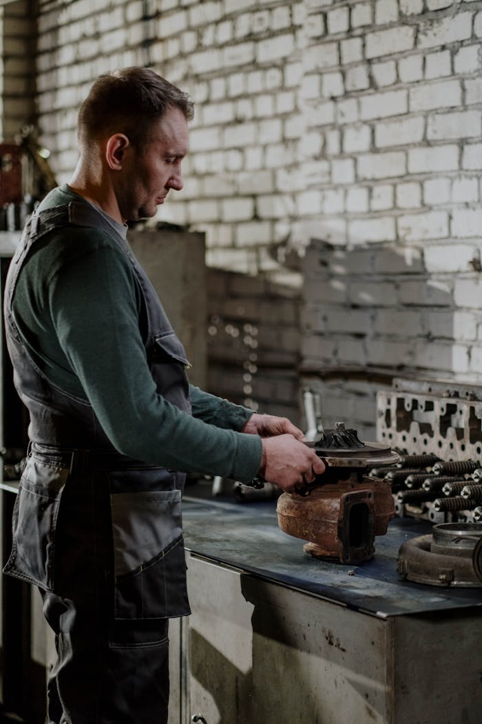 Mechanic focused on repairing a car engine part in an indoor workshop setting.