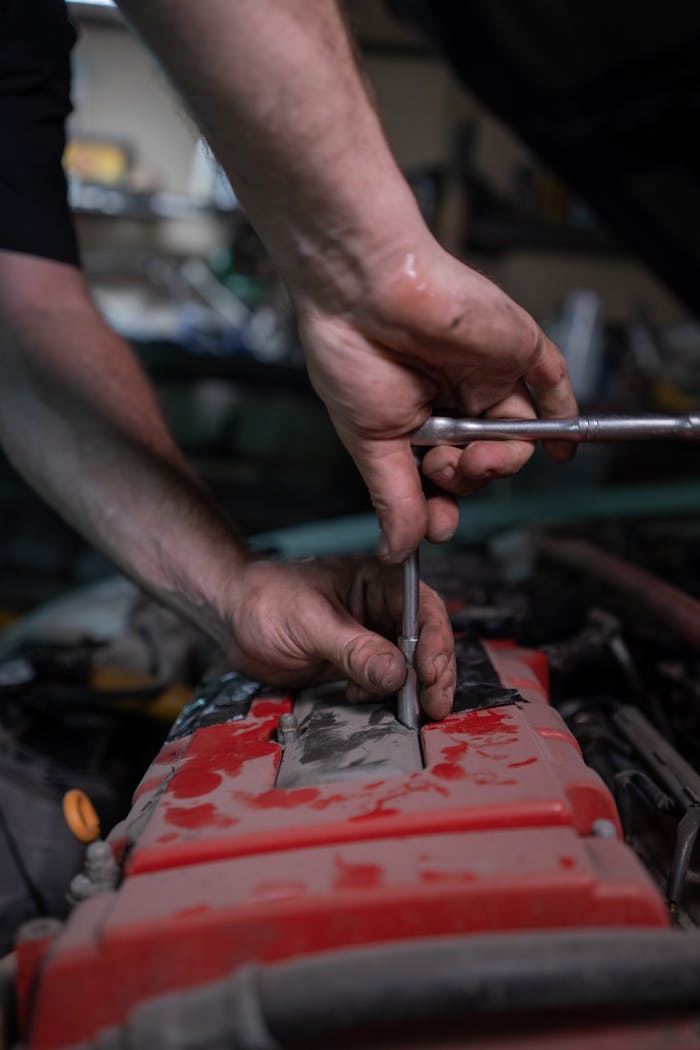A mechanic uses a socket wrench to repair a car engine in a garage setting.